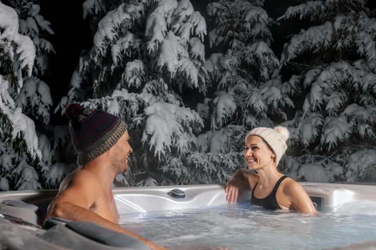 happy couple relaxing in outdoor hot tub at winter with snowy trees in background. spa resort